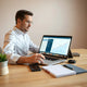 Small business owner reviewing laptop analytics with upward trend charts and blank notes