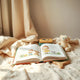 Open kids’ storybook on a blanket with a few colorful books and a plush toy nearby