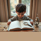 Child reading a mystery book with a magnifying glass and small clues on a table