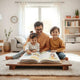 Parent and children sit together reading an open book in a bright, cozy living room.